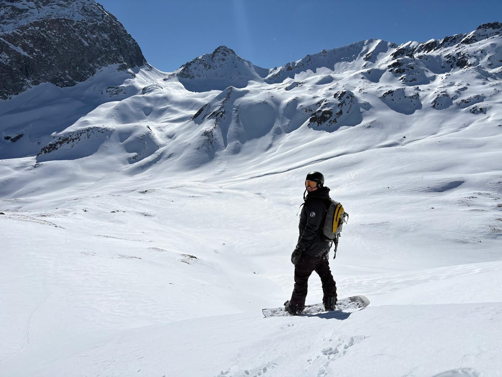 Robin Heer mit Snowboard und Rucksack im unverspurten Gelände, dahinter verschneite Hänge und Felsgrate.