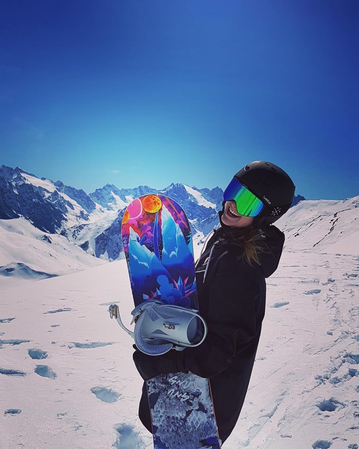 Melanie Meier, Mitgründerin von SnowRabbit, mit Snowboard vor verschneiten Alpengipfeln